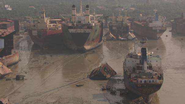 Carcasses of dismantled boats on the seafront, workers at work